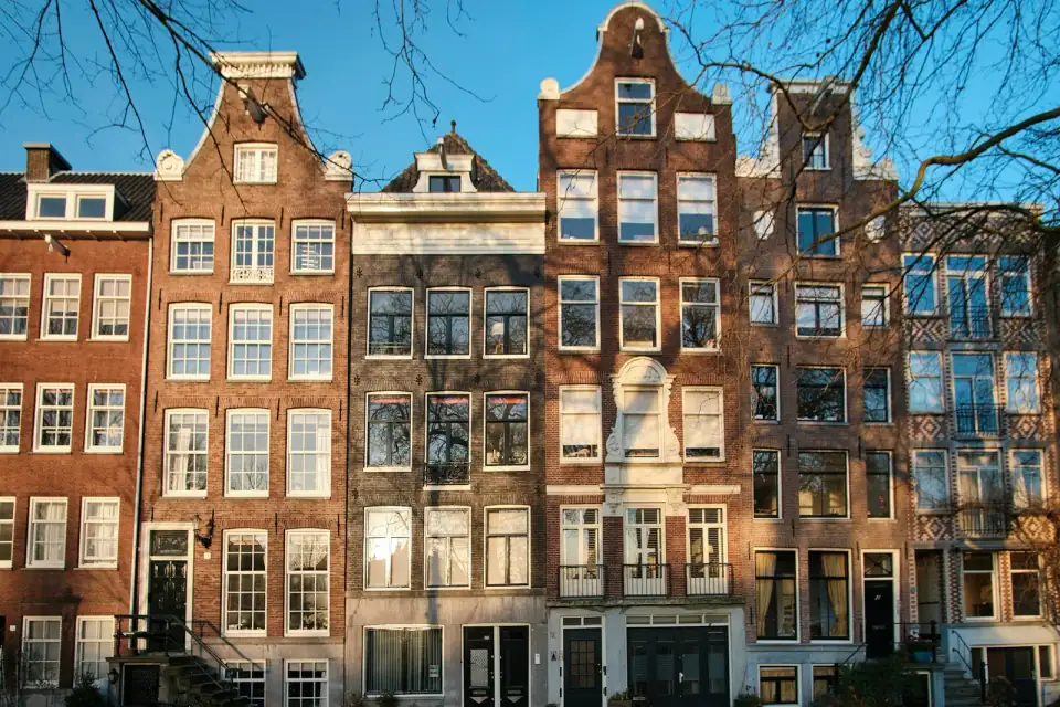 Rij oude grachtenpanden met trapgevels en witte kozijnen, in de winterzon