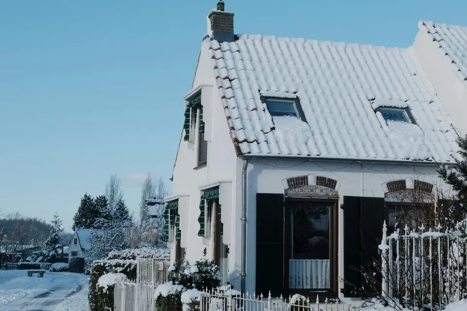 Wit huis met een pannendak vol sneeuw en groene luiken, aan een besneeuwde weg in Nederland