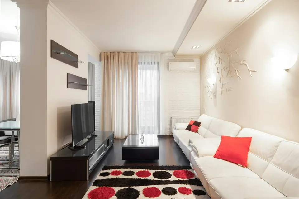 Woonkamer met een witte leren bank, lange gordijnen en een binnenunit van een airco hoog op de muur bij het raam